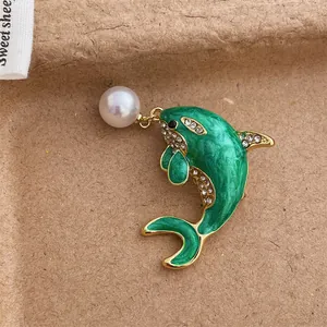 Macro detail of green enamel dolphin brooch with white rhinestones and a hanging pearl