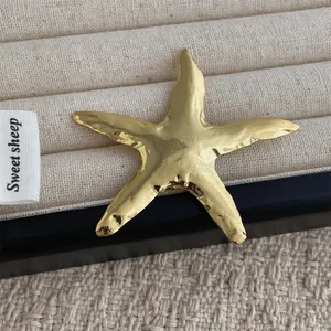 Macro shot of gold starfish brooch with textured wave pattern on a beige tray