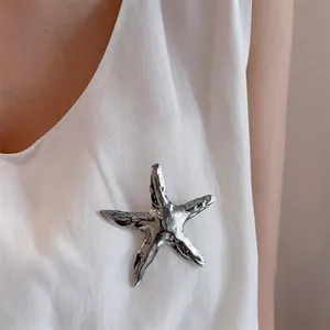 Detailed view of a silver starfish brooch with textured surface on a white V-neck garment