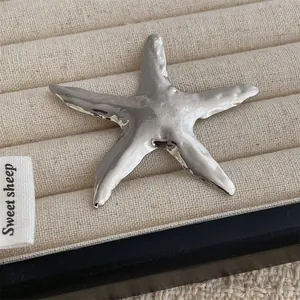 Elegant silver starfish brooch with textured metallic finish on a beige jewelry display