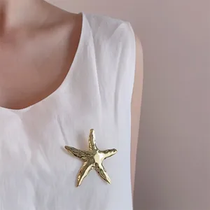 Detailed view of a gold starfish brooch with textured finish on a white linen shirt