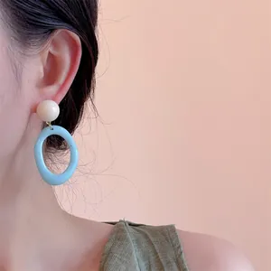 Detail of retro resin earrings with cream stud and light blue oval pendant on model