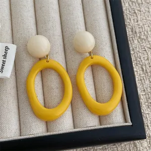 Detail of yellow oval resin pendant earrings displayed in a beige jewelry box