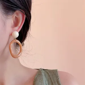 Close-up of resin drop earrings with cream beads and translucent amber hoops on model