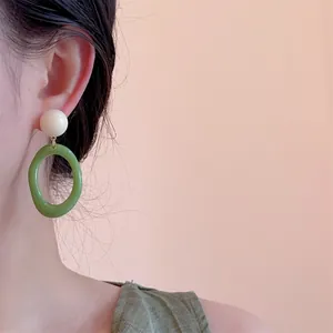 Close-up of retro color-block resin earrings with cream circle and green oval hoops