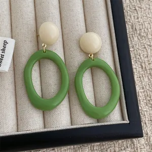 Detail of retro resin hoop earrings with beige studs and green oval pendants on fabric