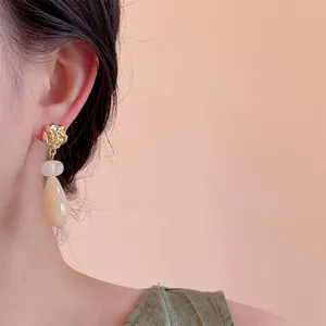 Détail du clou d'oreille floral avec pendentif goutte sur modèle avec fond rose doux