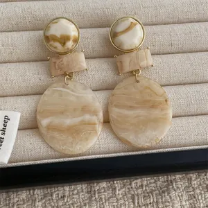 Detail of marble-textured resin drop earrings in cream and beige with gold metal links