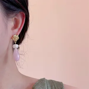 Détail de la boucle d'oreille goutte rose avec rose dorée et perle sur modèle