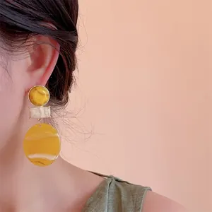 Detail of candy-colored marble resin earrings worn on a model against a soft pink backdrop