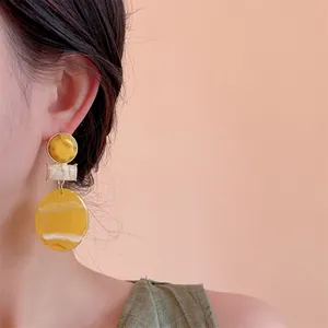 Close-up of a three-tier marble resin earring featuring yellow and cream geometric shapes
