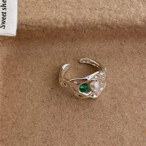 Detailed close-up of an irregular silver ring with green gemstone and white pearl inlay