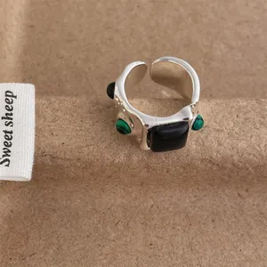 Macro shot of silver ring featuring square black stone and green gemstone accents