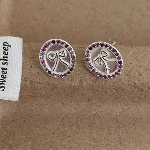 Detailopname van zilveren ovale oorbellen met paarse zirkonia en strik-accent