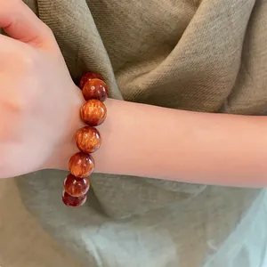 Dettaglio macro del bracciale con perle marroni e riflessi occhio di gatto su stoffa verde
