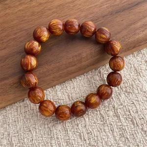 Dettaglio macro del bracciale con perle marrone-rossastre e trama dorata su legno
