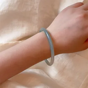 Macro detail of a translucent light green jade style bangle worn on a woman's wrist