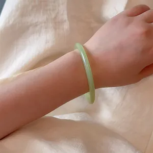 Close-up of a minimalist light green jade style bangle with a smooth polished finish