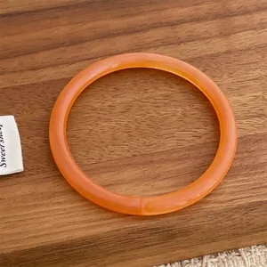 Close-up of a translucent orange resin bangle on a dark walnut wood surface