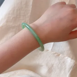 Close-up of a pale green jadeite bangle with smooth texture on a linen background