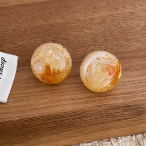 Handmade clear resin stud earrings with yellow dried flowers and gold foil on wood