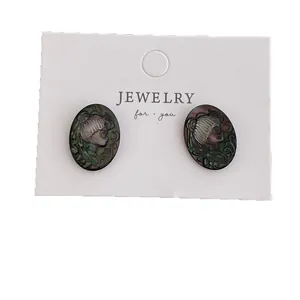 Oval earrings with black shell relief portrait carvings shown on a display card