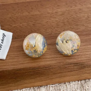 Detailed macro view of clear resin ball earrings with dried flowers and gold foil accents