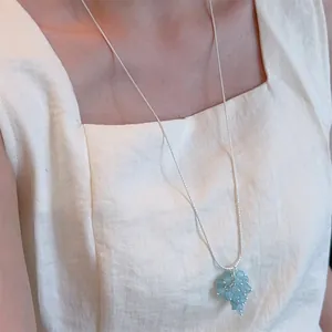 Detail of adjustable long necklace with a light blue grape bead pendant on beige dress