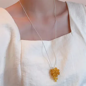 Close-up of vibrant yellow grape-shaped beaded pendant on long silver sweater chain