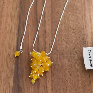 Detail showing yellow grape cluster beads on a silver snake chain over wood