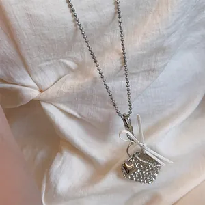 Detail van zilveren hart hanger met wit lint op kralenketting voor damestruien