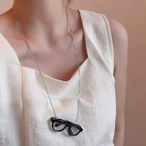 Detail view of a silver necklace with a minimalist black round frame glasses pendant