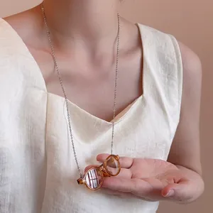 Detailed close-up of a long silver chain necklace with a mini amber round glasses pendant