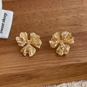Macro detail of gold flower earrings with brushed texture and sparkling zircon petals
