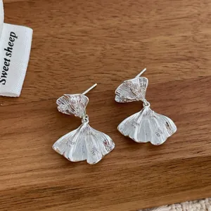 Macro shot of silver ginkgo leaf earrings with crystal accents on a wooden display