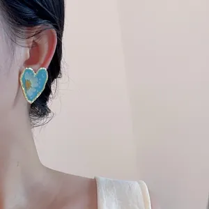 Detail of heart-shaped earring featuring white daisy floral resin inlay on ear