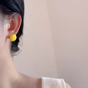 Close-up of bright lemon yellow round stud earring worn on ear with glossy finish