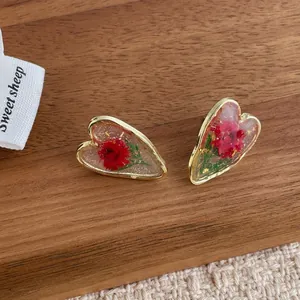 Handmade heart resin earrings with red dried flowers and gold foil on wooden background