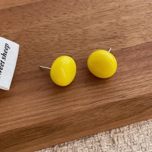Close-up of vibrant yellow button stud earrings on wood and cream fabric background