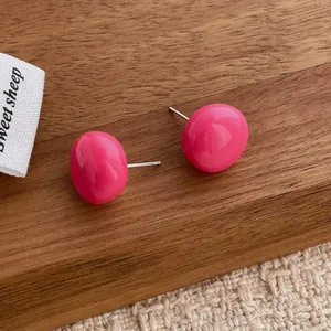 Detailed macro view of rose pink dome stud earrings on a textured wooden background