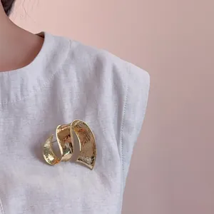 Détail de la broche ruban doré avec finition martelée sur une veste en lin gris clair