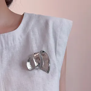 Élégante broche ruban en métal martelé argenté sur une veste sans manches chic
