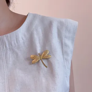 Elegant 18K gold plated dragonfly brooch on a grey garment with hammered texture