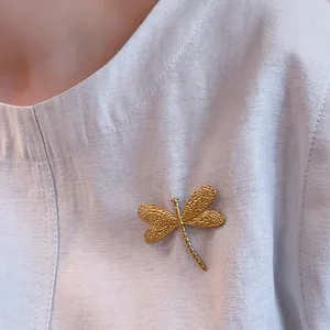 Macro shot of 18K gold-plated dragonfly brooch with textured wings on fabric
