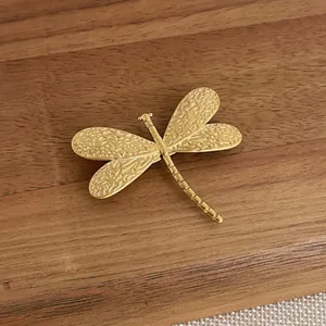 Detailed view of matte gold dragonfly brooch with vintage relief texture on dark wood