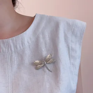Detailed close-up of a silver dragonfly brooch with textured wings on grey fabric