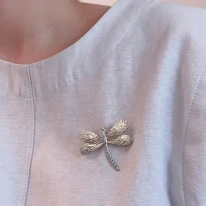 Silver dragonfly brooch with hammer-textured wings on a light blue suit jacket