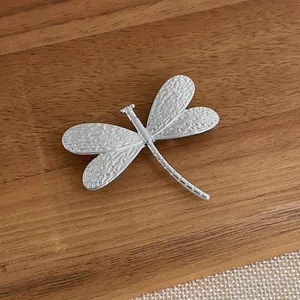 Silver dragonfly brooch with 18K gold plating and textured wings on a dark wood surface