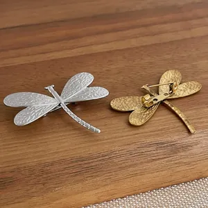 Detailed view of gold and silver dragonfly brooches with hammered metal texture