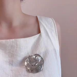 Broche circulaire argentée avec texture martelée et perle sur un vêtement beige